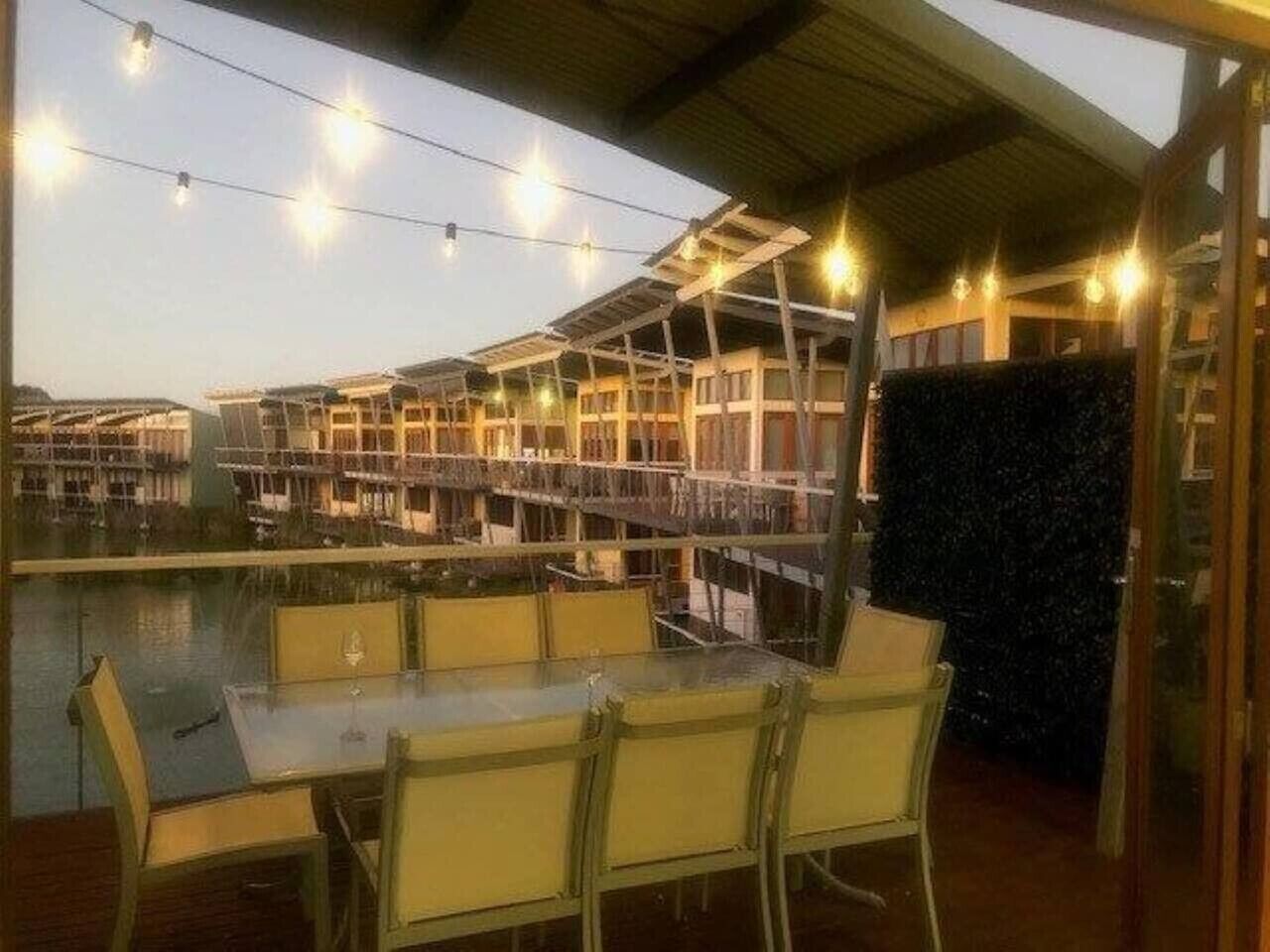 An outdoor dining area with a pool view, covered seating, and string lights.