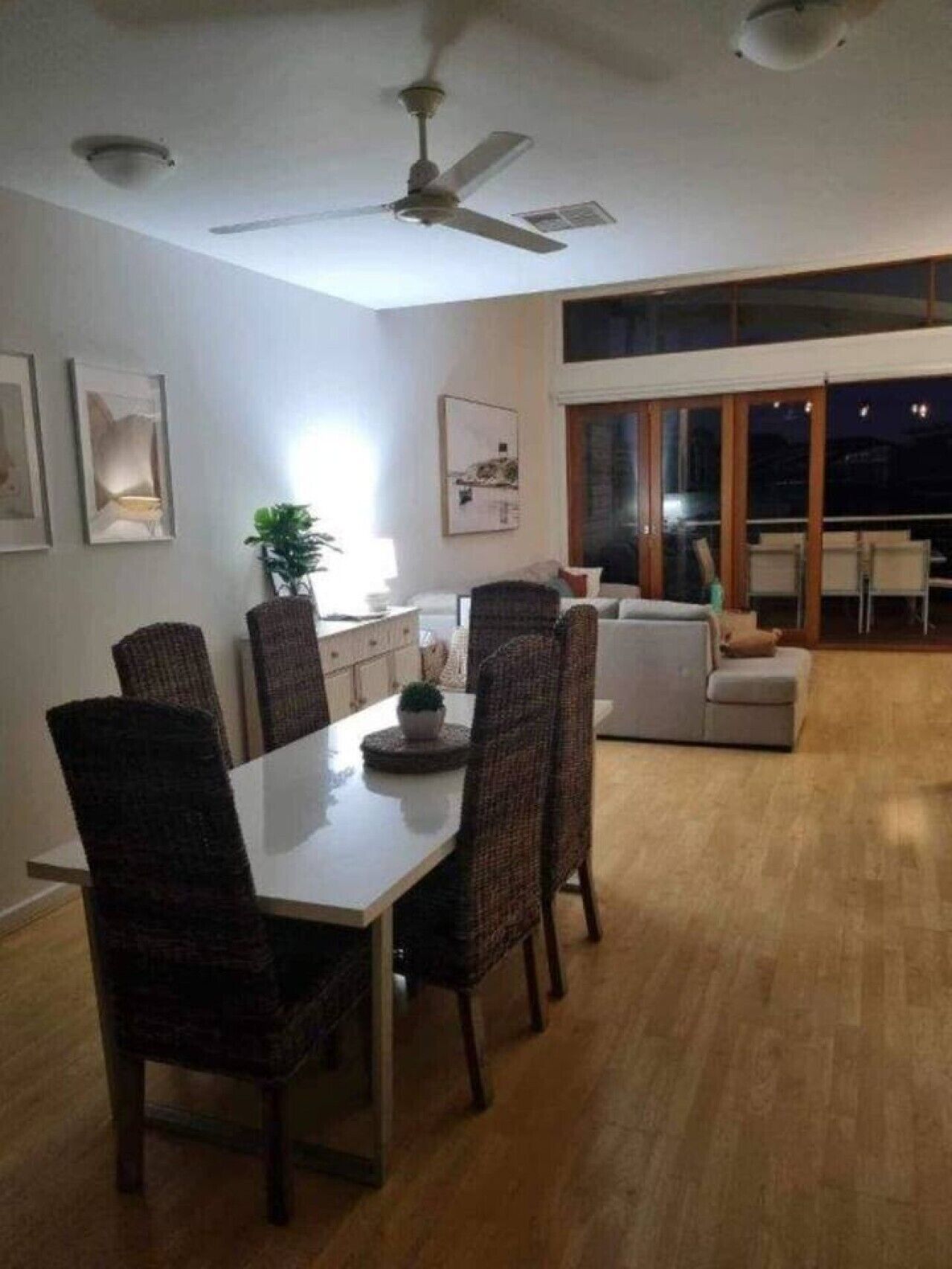 Un comedor con una mesa y sillas, un ventilador de techo y vistas al exterior a través de amplios ventanales.