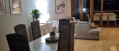 Un comedor con una mesa y sillas, un ventilador de techo y vistas al exterior a través de amplios ventanales.