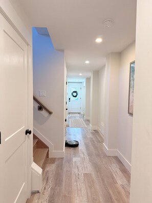 A hallway with a wooden floor, white walls, a door with a black handle, and a light fixture on the ceiling. - 3000 sq. ft, 4-BR, 4 Bath, 3 Blocks to the ocean beach house in Seaside Heights. (Seaside Heights)