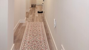 Um corredor com tapete estampado, luminária no teto e porta no final.