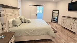 Quarto com uma cama grande, cômoda, espelho e televisão na parede.