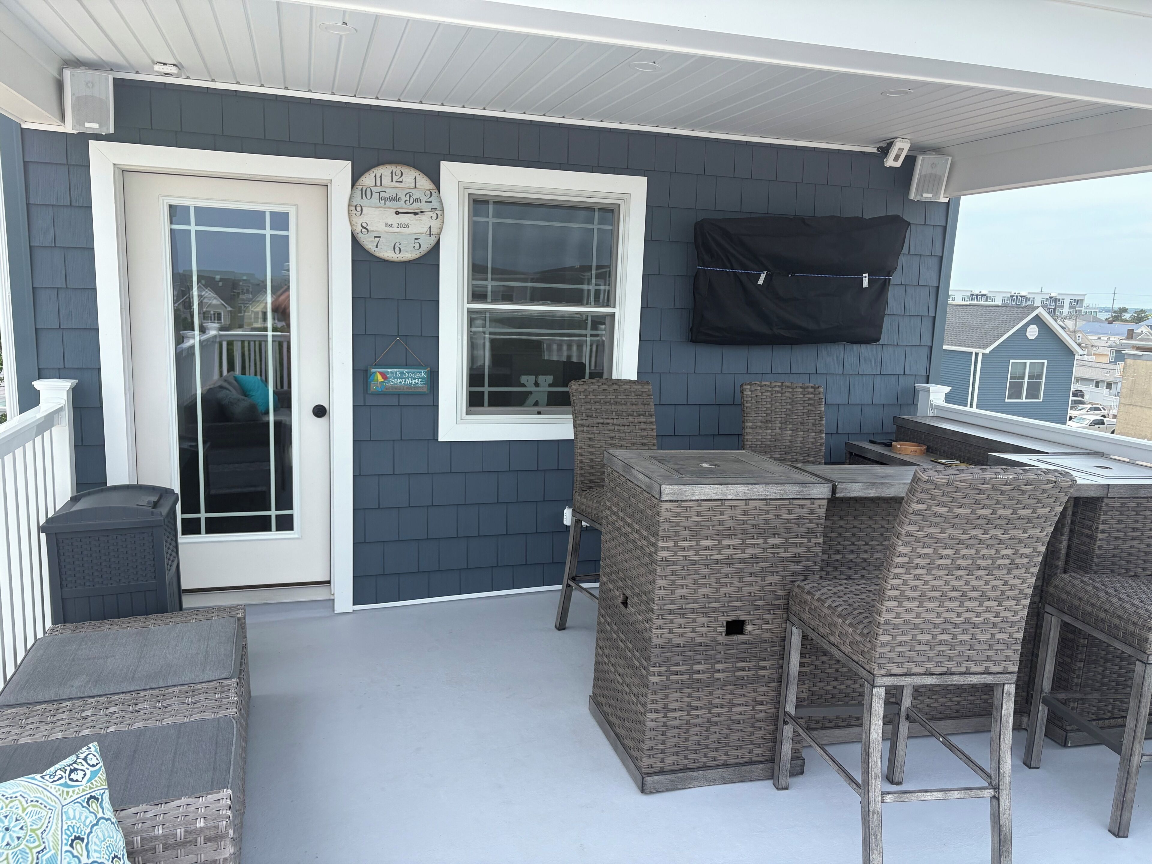 A covered porch with wicker furniture, a clock, and a view of the neighborhood.