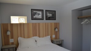 Habitación de hotel con cabecera de madera, dos mesitas de noche, cama con sábanas blancas, dos cuadros en la pared y un perchero.