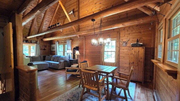 A wooden cabin interior with a dining area, sofa, and fireplace. - Highlands Hideaway - Secluded 4BR Forest Gem (Roaring Branch)