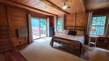A wooden cabin bedroom with a bed, a dresser, and a window.