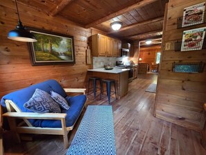 Interior de una cabaña con comedor, cocina y sofá con cojines.