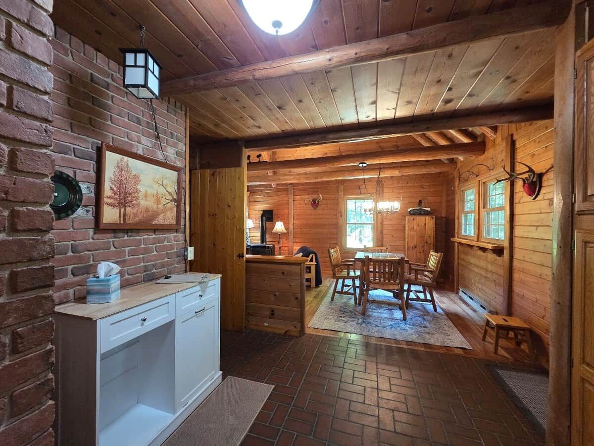 Un interior de madera con comedor, una cocina con armario blanco y una pared de ladrillo.