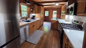 A wooden cabin interior with a kitchen featuring a stainless steel refrigerator, a stove, and wooden cabinets. - Highlands Hideaway - Secluded 4BR Forest Gem (Roaring Branch)