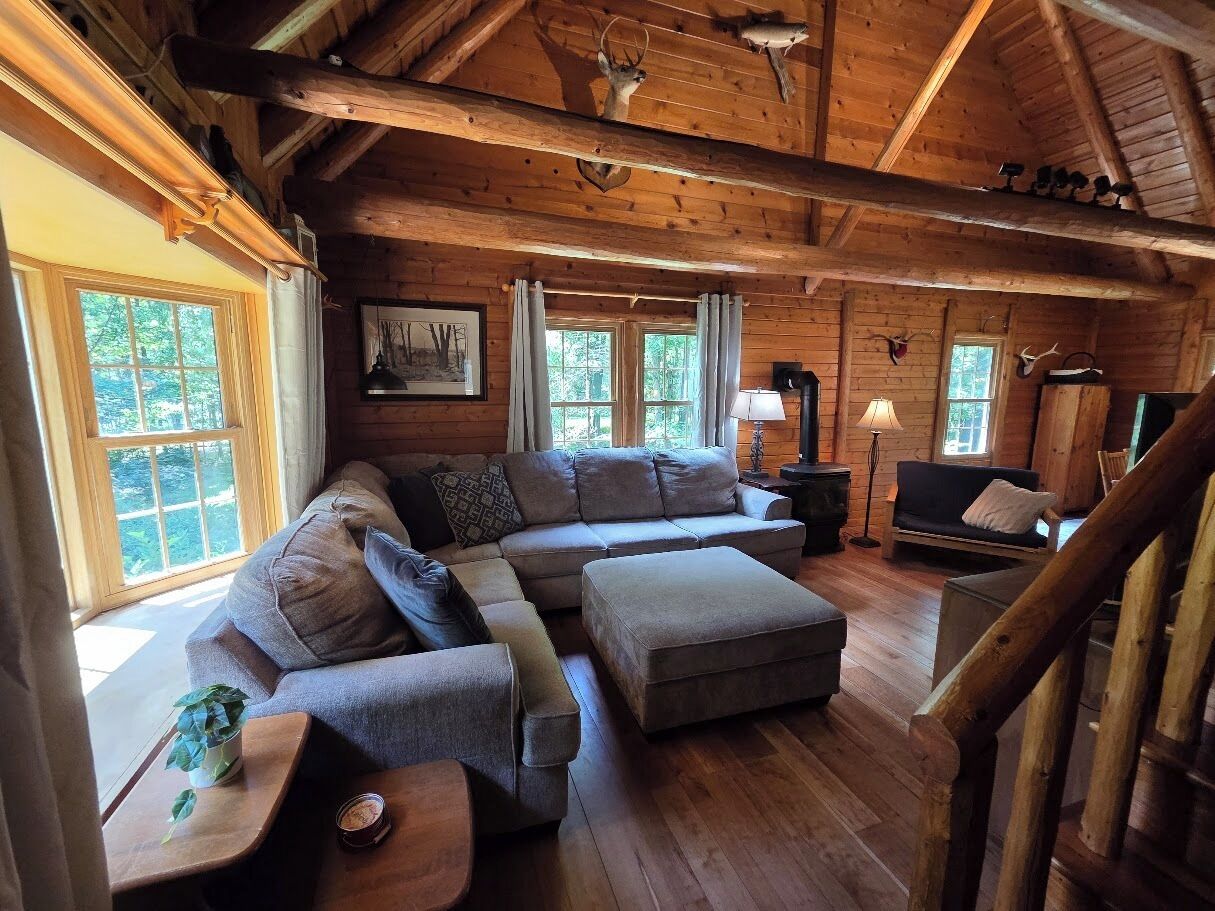 L'intérieur d'une cabane en rondins, avec un canapé d'angle, un pouf et une cheminée.