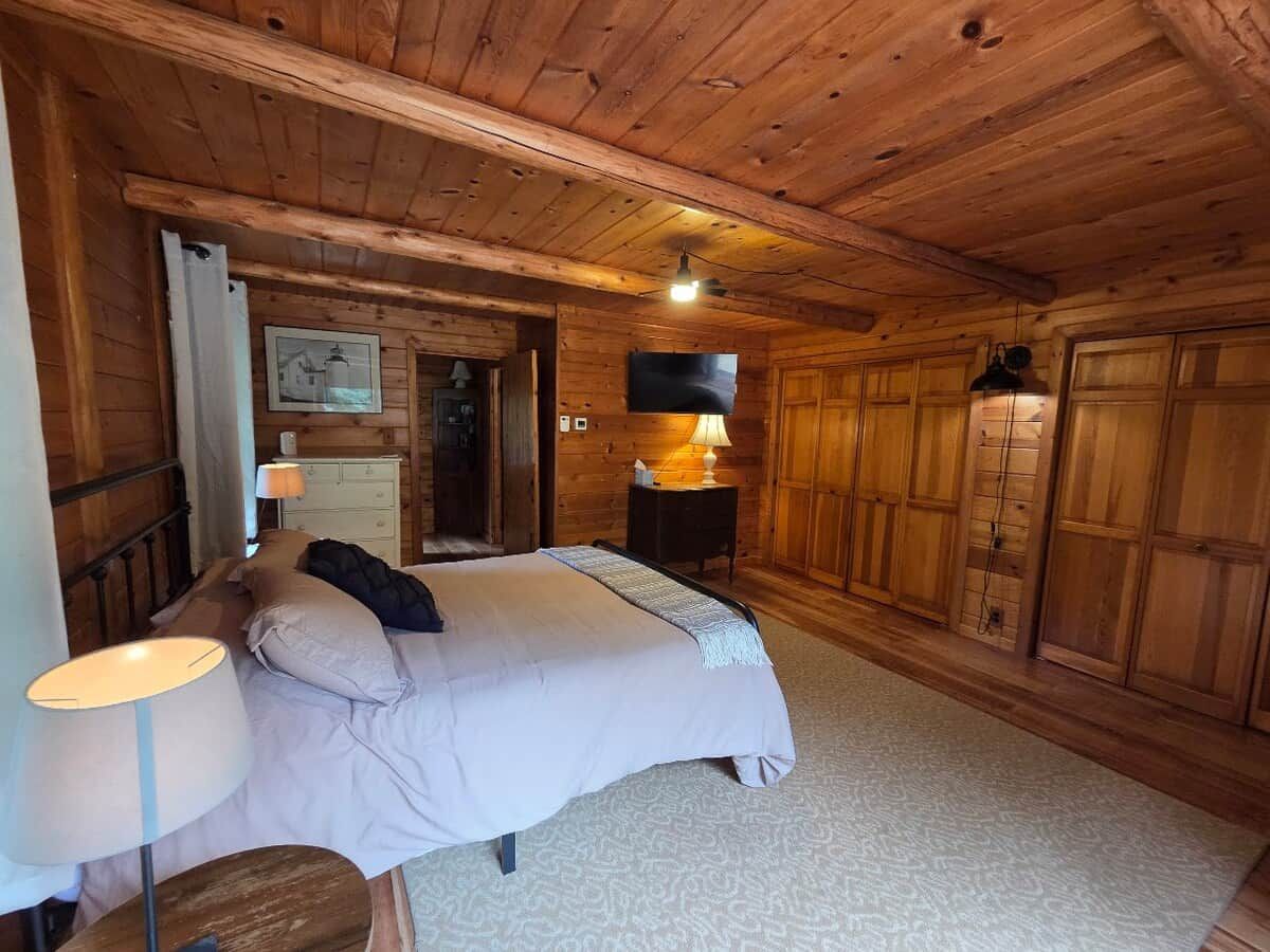 Dormitorio de cabaña de madera con cama, mesita de noche, lámpara y armario.