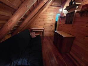 Un cuarto ático acogedor con techo inclinado de madera, un sofá negro, una mesita y un armario de madera.