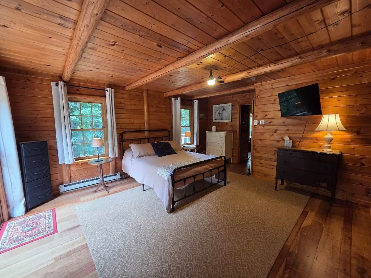 A wooden cabin bedroom with a bed, dresser, and a TV mounted on the wall.