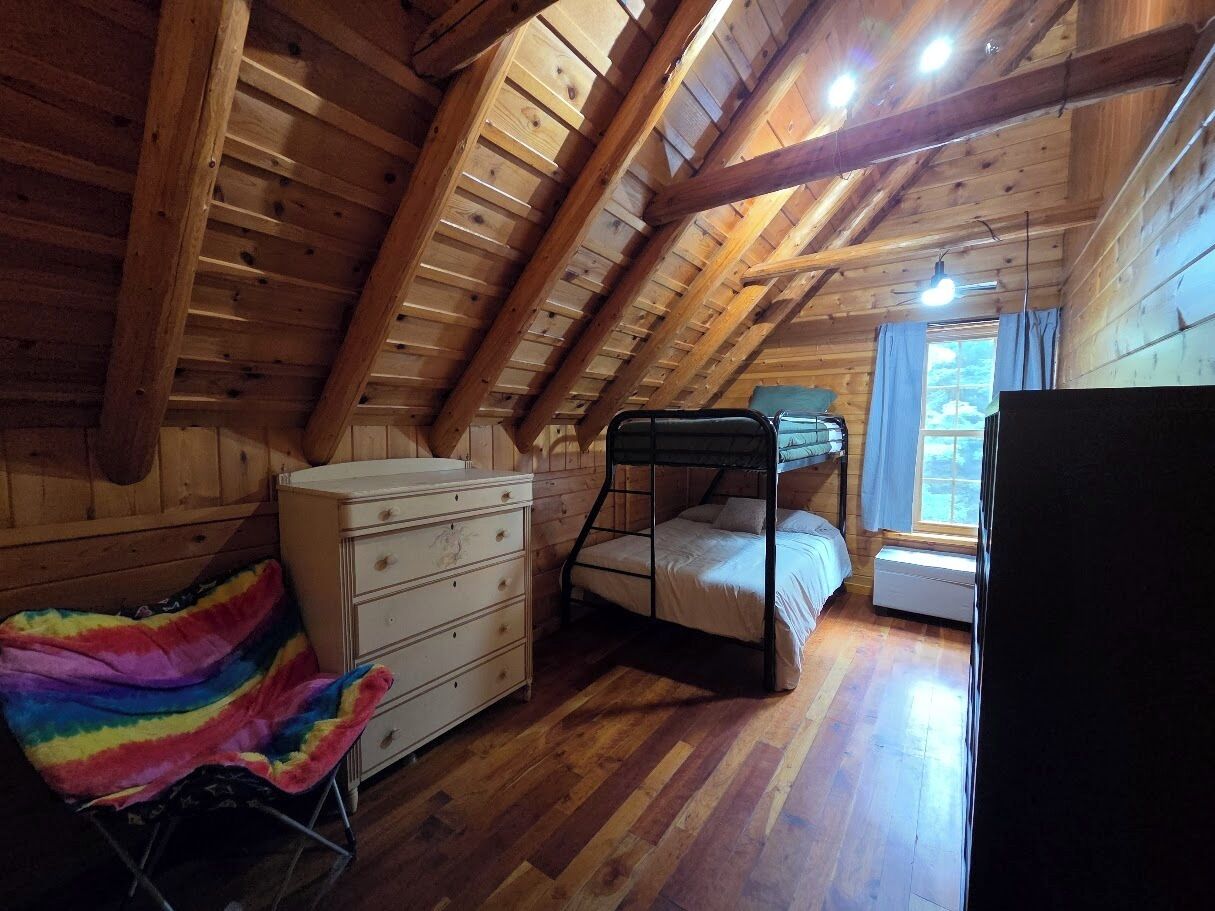 A wooden attic bedroom with a bunk bed, dresser, and a colorful blanket.