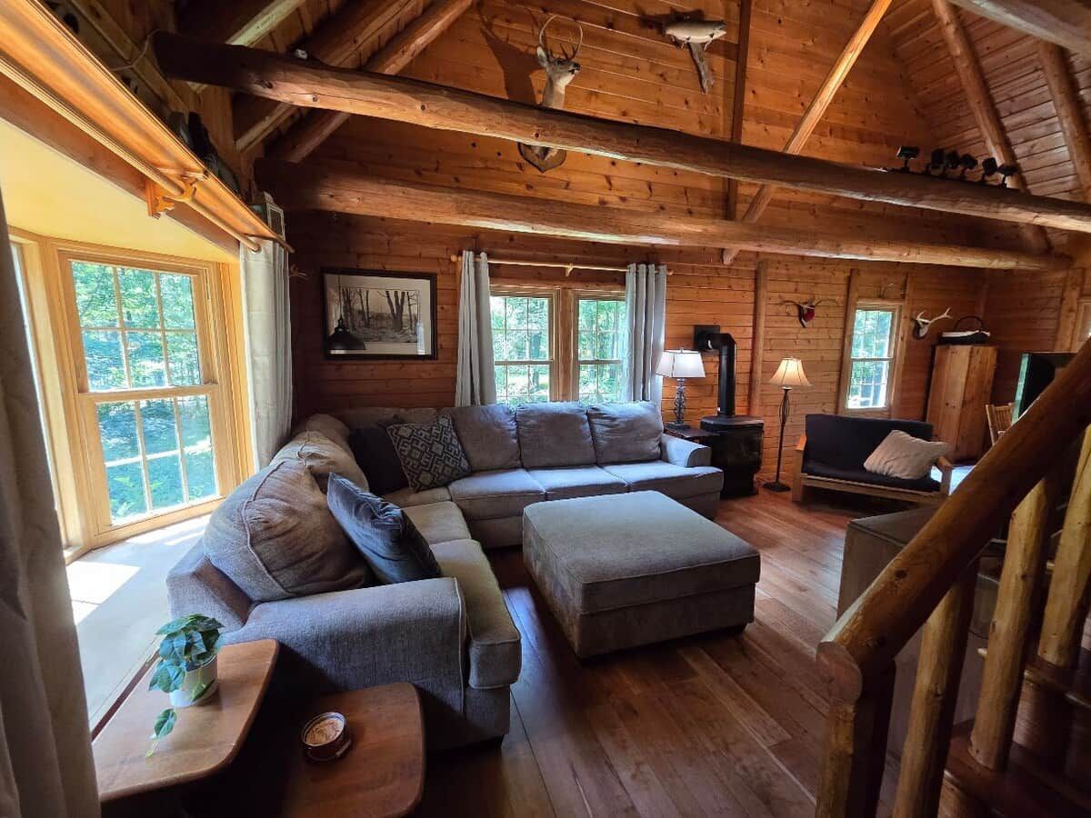 A log cabin interior with a sectional sofa, ottoman, and a staircase.