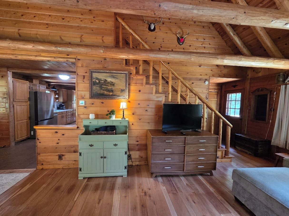 L’intérieur d’une cabane en bois comprend une cuisine, un escalier, un téléviseur et un meuble vert.