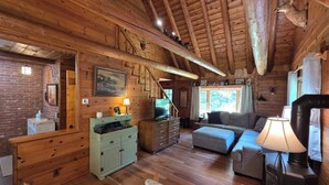 A wooden cabin interior with a fireplace, a sofa, a television, and a staircase. - Highlands Hideaway - Secluded 4BR Forest Gem (Roaring Branch)