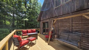 A wooden deck with outdoor seating, a ladder, and a large window. - Highlands Hideaway - Secluded 4BR Forest Gem (Roaring Branch)