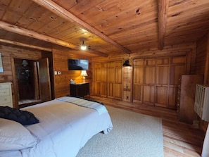 Interior de una cabaña de madera con una cama, una mesita de noche, una lámpara y un armario.