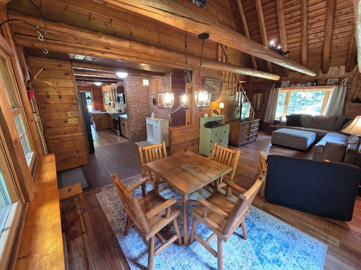A wooden interior with a dining table, chairs, a sofa, and a kitchen area.