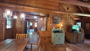 A rustic wooden interior with a dining table, chairs, a staircase, and a television. - Highlands Hideaway - Secluded 4BR Forest Gem (Roaring Branch)