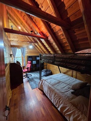 Una habitación pequeña y acogedora con techo inclinado, una cama litera, un escritorio con silla y una ventana con cortinas.