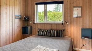 Ein Zimmer mit Holzwänden, einem Bett, einem Fenster, einem Schreibtisch und einem Regal.