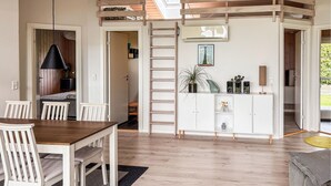 Ein modernes Interieur mit einem Holztisch, weißen Stühlen, einer weißen Schrankwand mit Regalen, einer Leiter und einem Oberlicht.