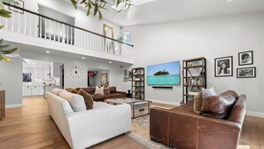 A spacious living room with a high ceiling, a balcony, a large flat-screen TV, and a bookshelf. - LA Times "Hot Property" l HGTV Resort Estate near Dana Point Harbor (San Juan Capistrano)