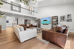 Ein geräumiges Wohnzimmer mit hoher Decke, einem Balkon, einem großen Flachbildfernseher und einem Bücherregal.