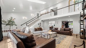 A spacious living room with a staircase, leather sofas, a coffee table, and a large rug. - LA Times "Hot Property" l HGTV Resort Estate near Dana Point Harbor (San Juan Capistrano)