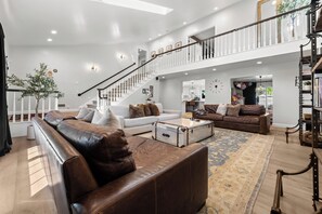 Ein geräumiges Wohnzimmer mit Treppe, Ledersofas, einem Couchtisch und einem großen Teppich.