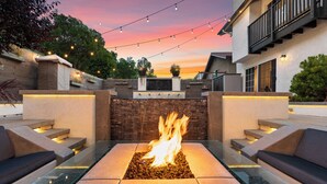 A fire pit in a square stone planter surrounded by glass-topped tables and benches. - LA Times "Hot Property" l HGTV Resort Estate near Dana Point Harbor (San Juan Capistrano)