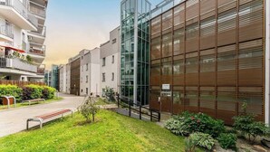 Een modern gebouw met een glazen gevel, een houten wandpaneel en een kleine tuin met bankjes.