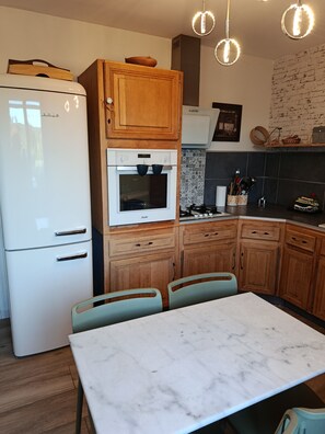 Eine Küche mit Kühlschrank, Backofen, Mikrowelle, Holzschränken und einem Marmortisch.