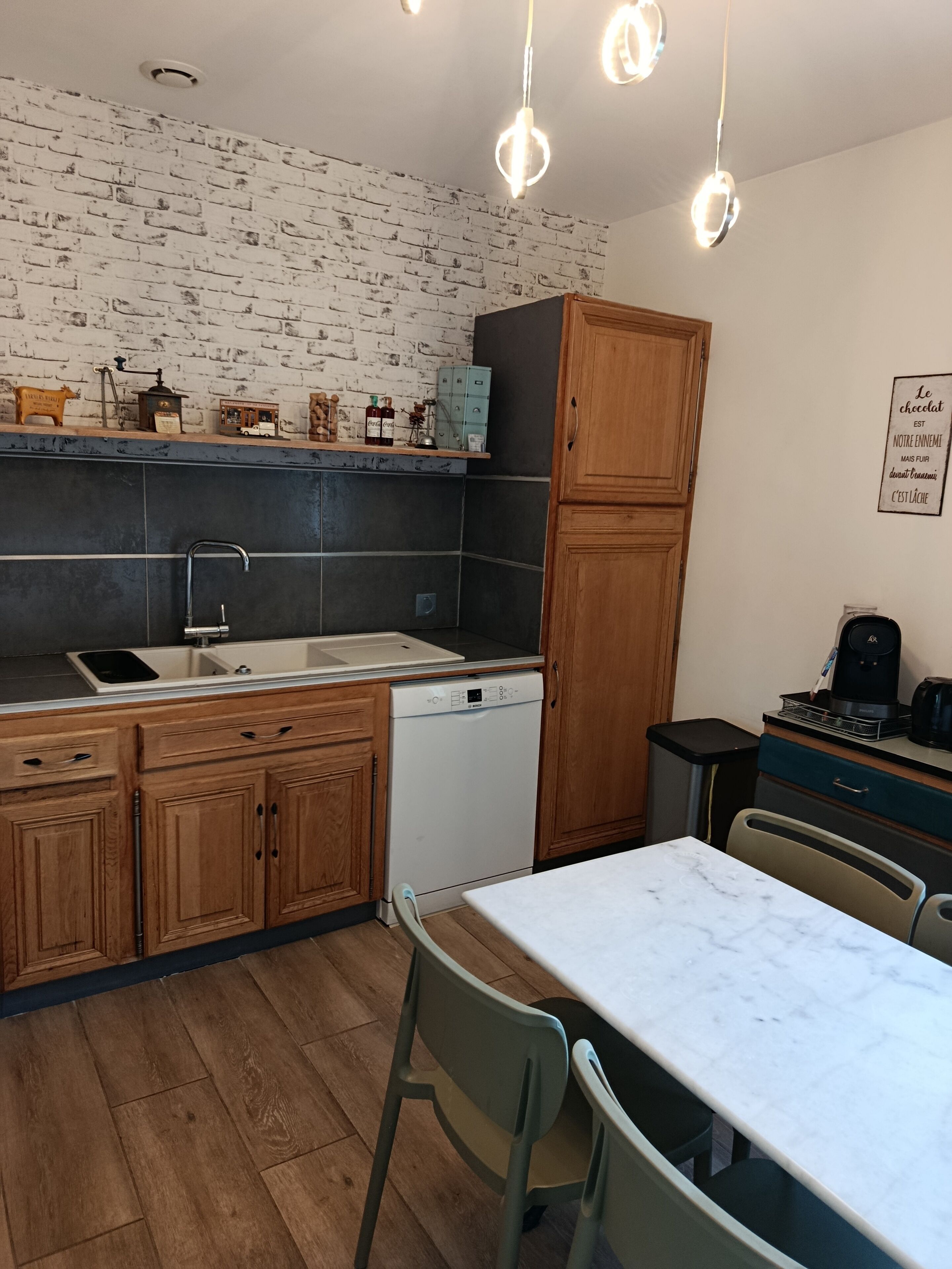A kitchen with a dishwasher, wooden cabinets, a marble countertop, and pendant lighting.