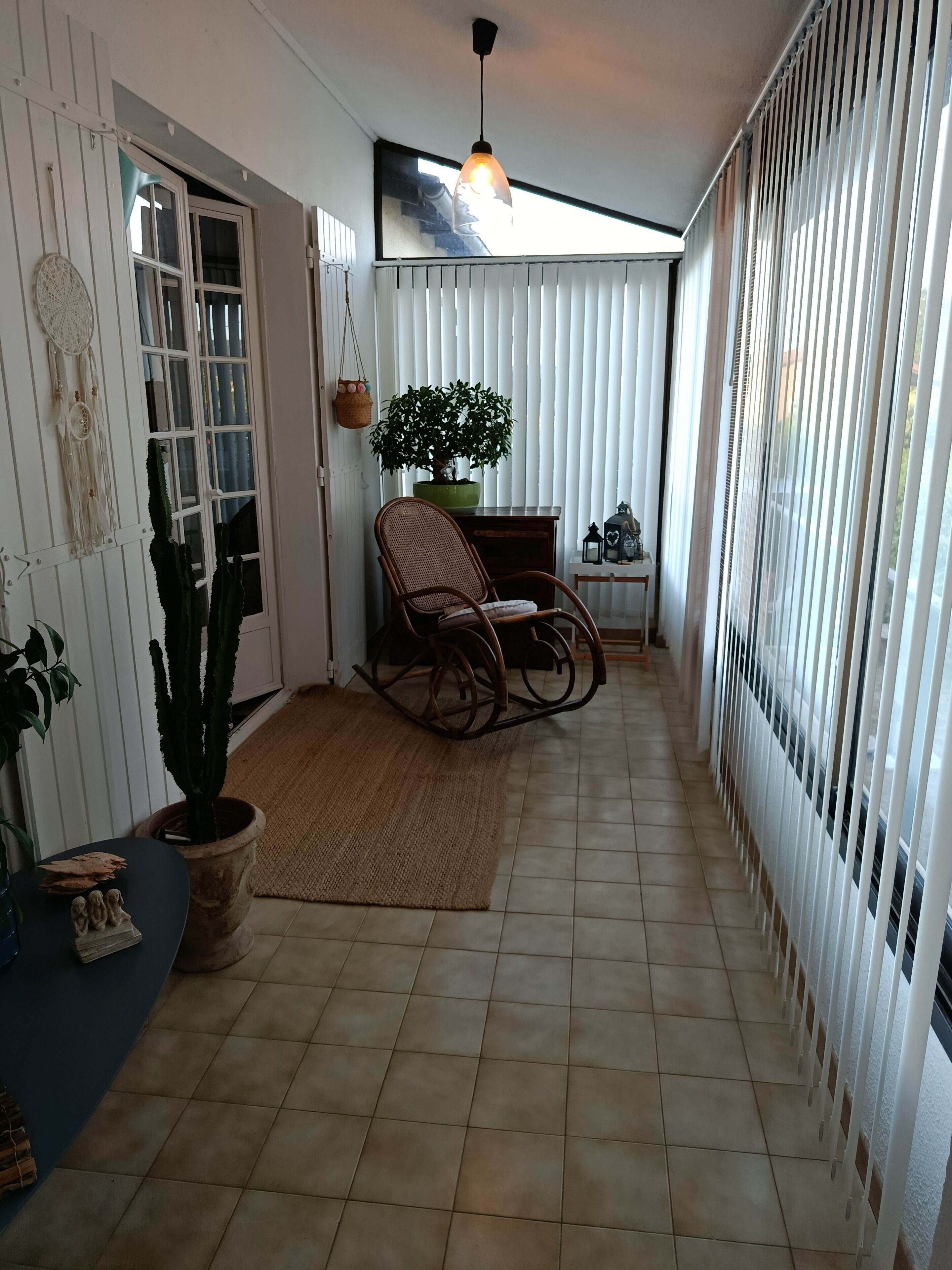 A corridor with a rocking chair, potted plants, and a hanging light fixture.
