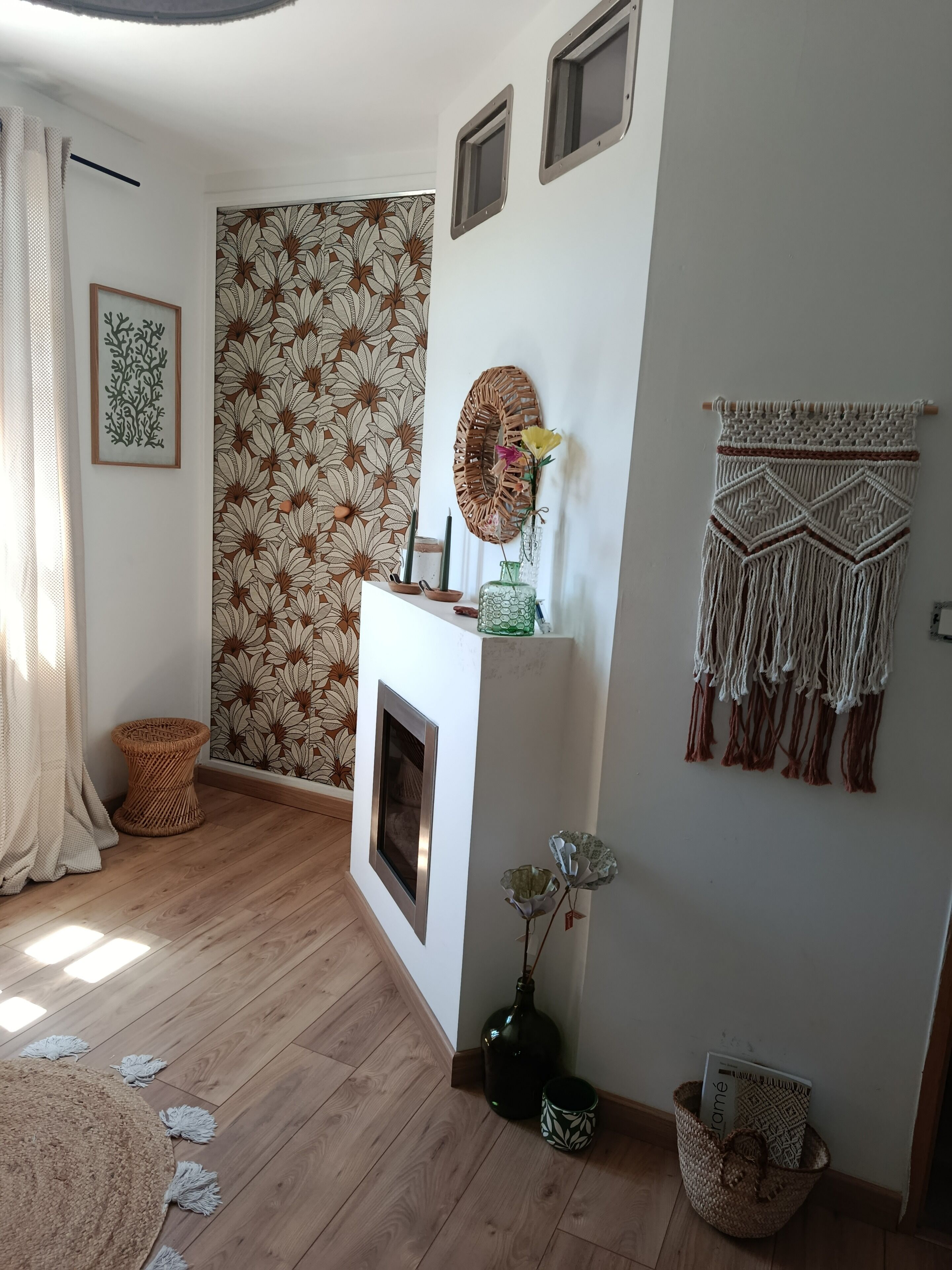 A room with a patterned wallpaper, a fireplace, a macrame wall hanging, and a woven basket.
