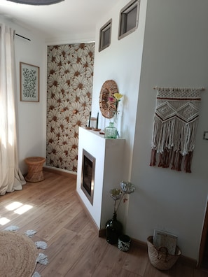A room with a patterned wallpaper, a fireplace, a macrame wall hanging, and a woven basket. - Time Regained (Saint-Martin-de-Valgalgues)
