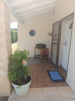 Ein überdachter Patio-Bereich mit einem Blumentopf, einem kleinen Tisch mit Plattenspieler und einer Tür mit Metallgitter.