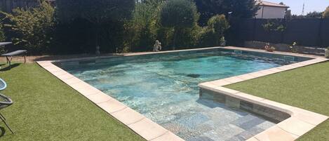 A rectangular swimming pool with clear water, surrounded by artificial grass and a stone border.