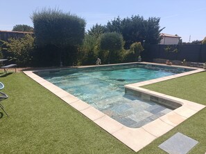 A rectangular swimming pool with clear water, surrounded by artificial grass and a stone border. - Time Regained (Saint-Martin-de-Valgalgues)