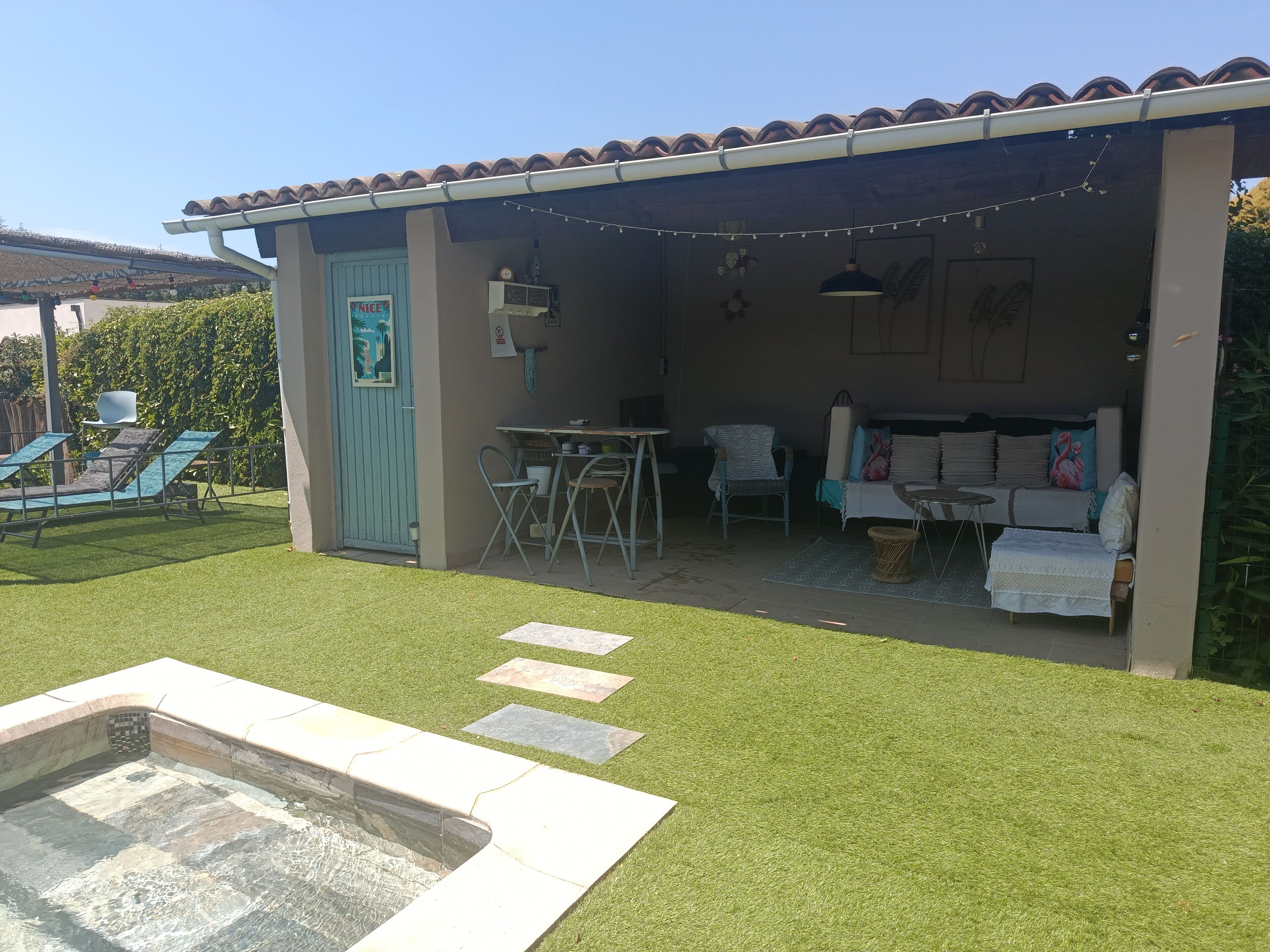 A covered outdoor seating area with a pool, lounge chairs, and a table.
