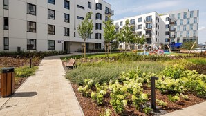 Un edificio moderno con diversi piani, un vialetto lastricato e aree verdi con arbusti e alberi.