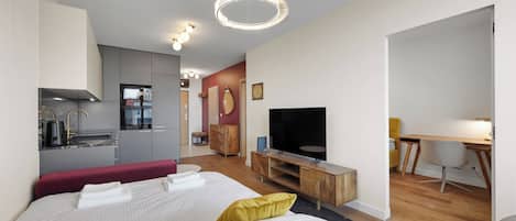 A modern hotel room with a bed, a TV, a desk, and a kitchenette.