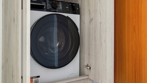 Huoneessa on etuaukollinen pesukone, ja siinä on puuovi sekä valkoinen seinä.