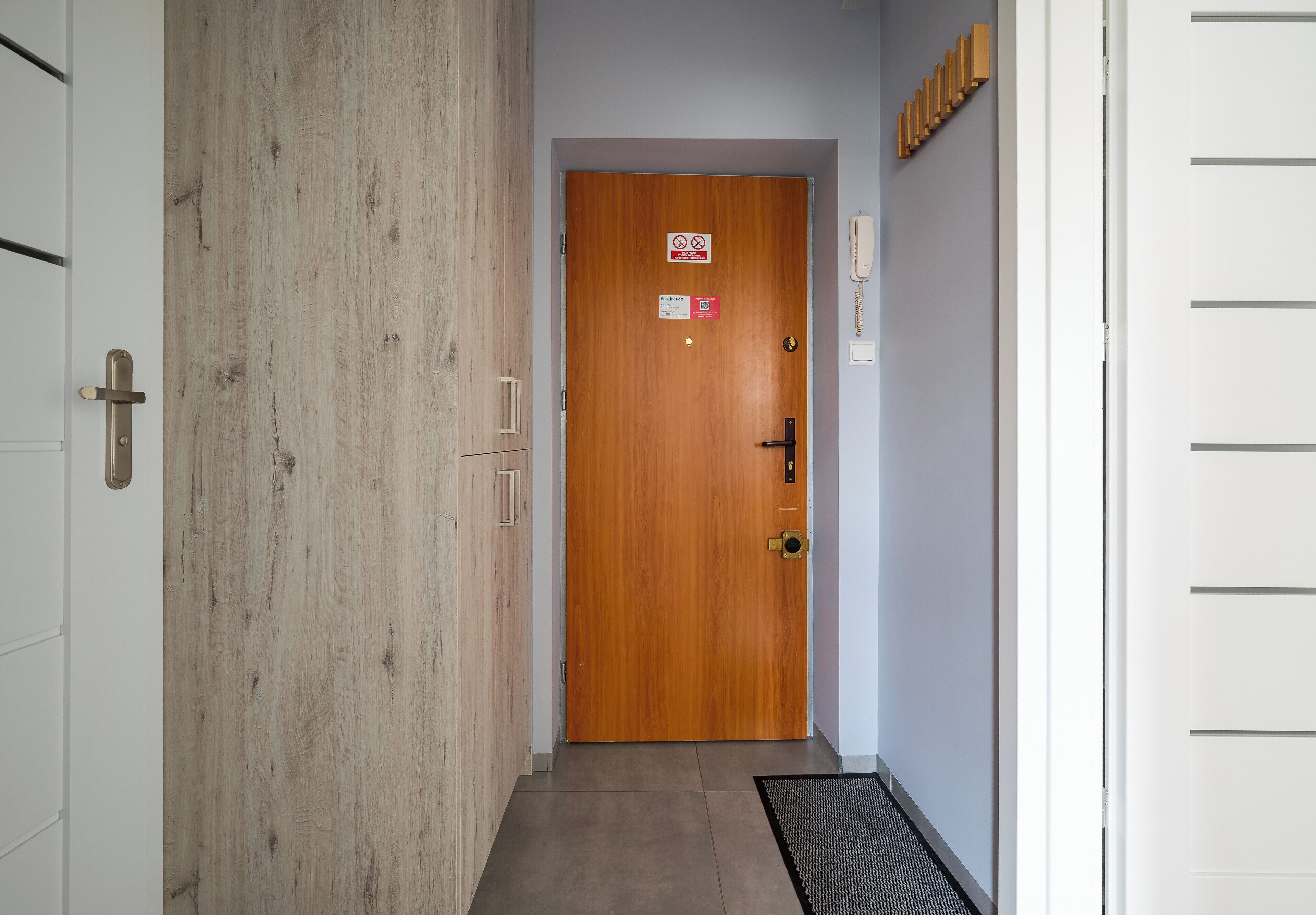 A hallway with a wooden door, a phone, and a mat.