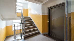 En trappe med metalgelændere, en elevator med glashæklåge, og en gul og hvid væg.