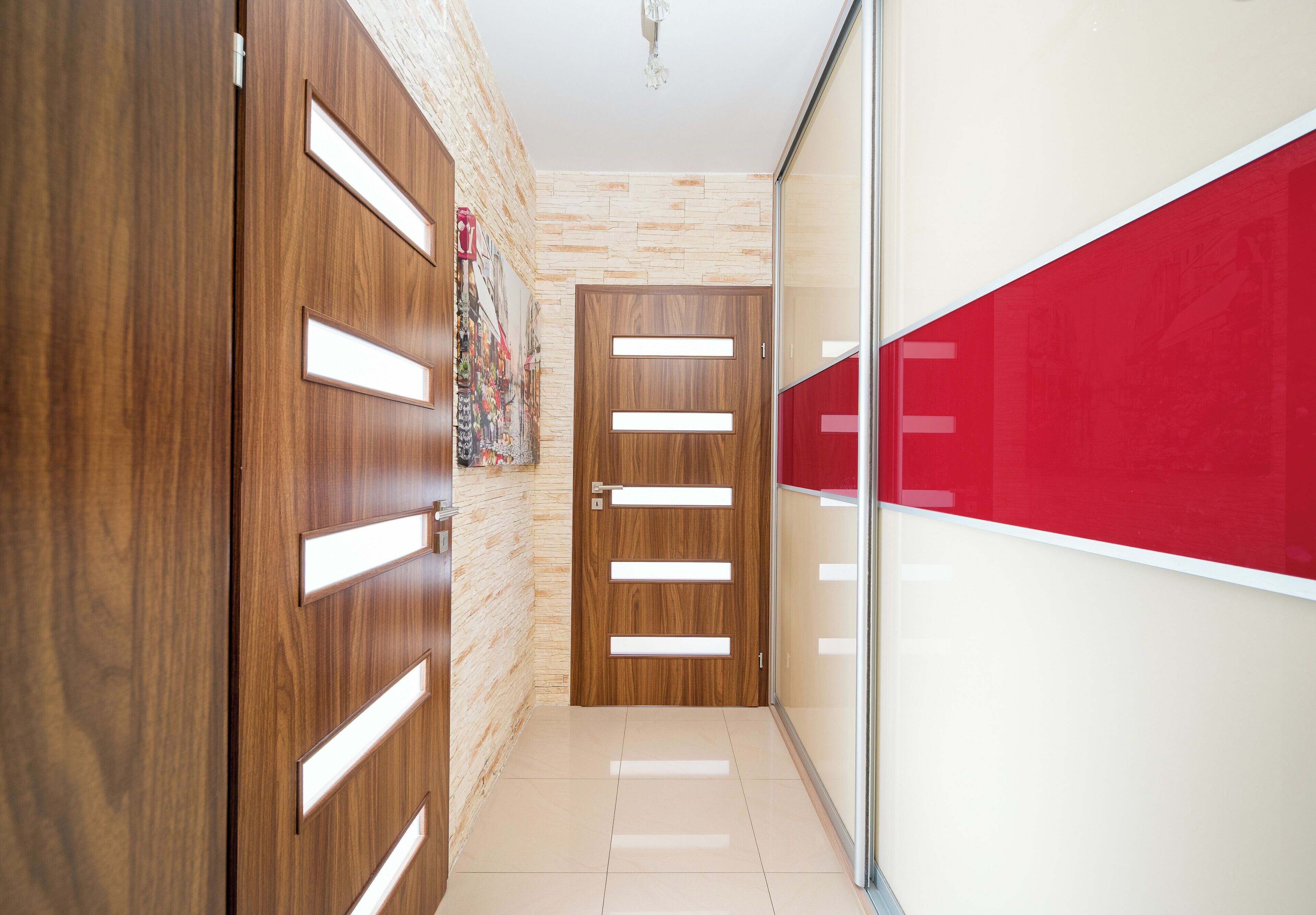Un corridoio con porte in legno, un muro rosso e un pavimento piastrellato.