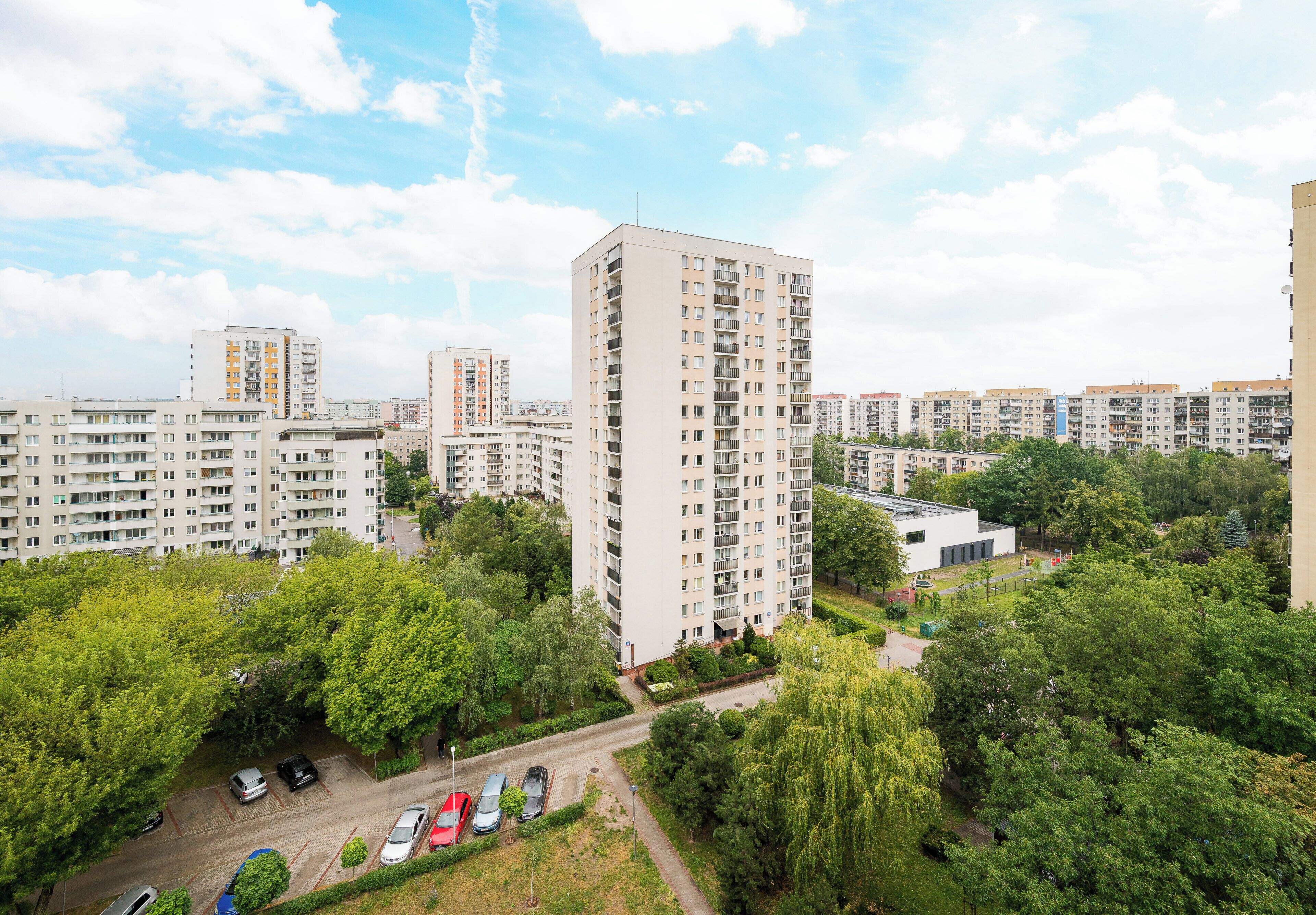 A high-rise residential building with multiple balconies, surrounded by greenery and other residential buildings.